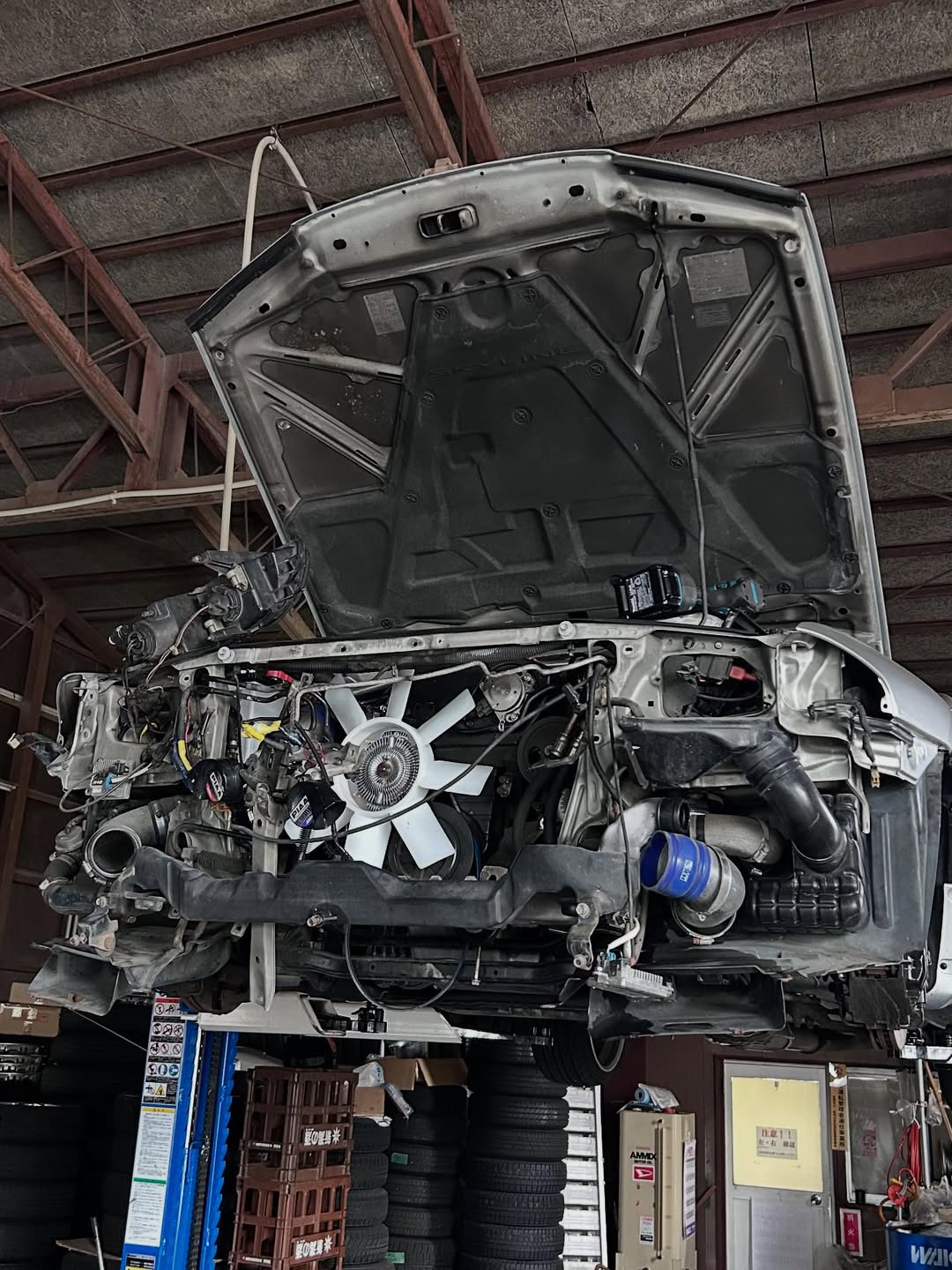 リフトアップされた日産スカイラインのエンジンルームを点検している様子。上越市ほしのじどうしゃの整備工場にて